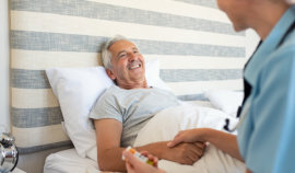 female caregiver holding the hand of senior man laying in bed